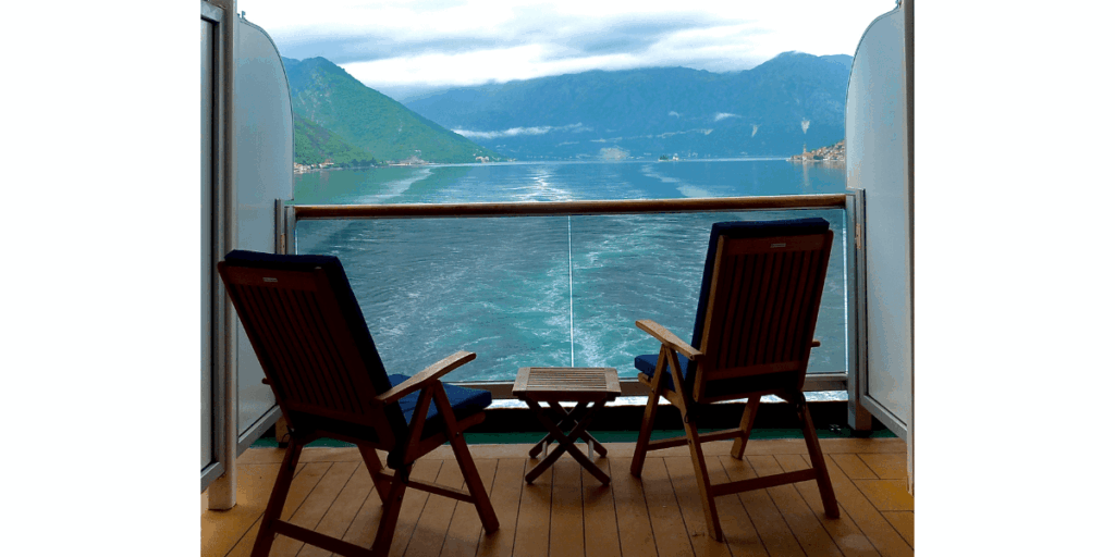 Two deck chairs on a cruise ship balcony overlooking calm water and distant green lush mountains.