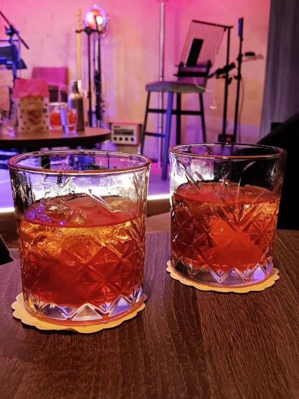 Close-up of two old-fashioned glasses filled with amber-colored cocktails, set against the softly lit backdrop of the 710 Club on P&O’s Iona, conveying an ambiance of leisure and evening entertainment.
