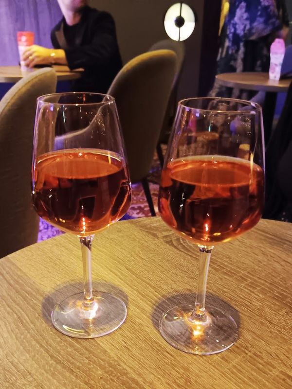 Two glasses of rose wine on a wooden table, with the soft focus of a lounge atmosphere in the background, highlighting a relaxed and sophisticated drinking experience at the 710 Club on P&O’s Iona.