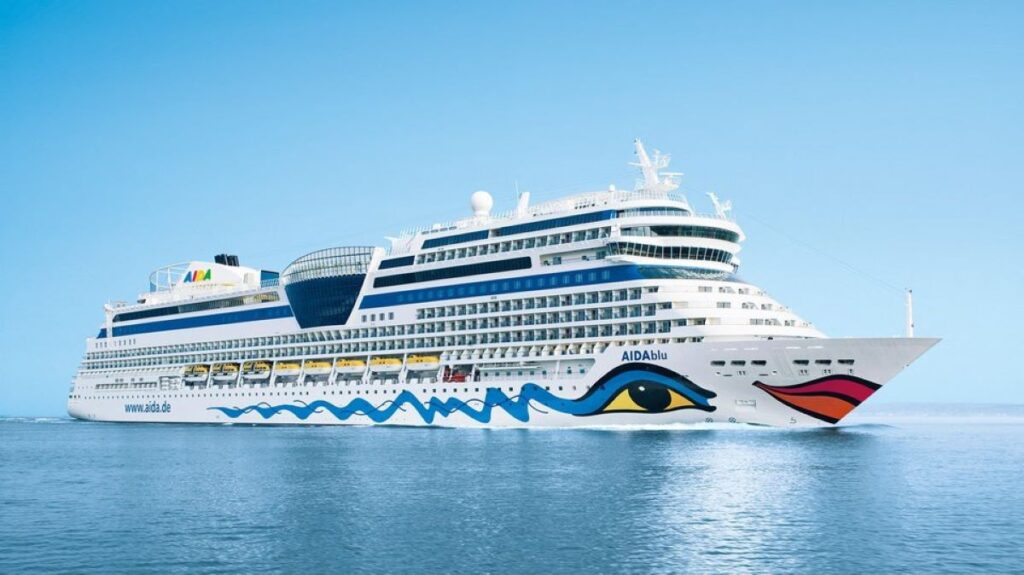 AIDA Cruises' AIDAblu cruise ship adorns the ocean with its distinctive art, featuring vibrant lips and eye motifs on the hull, set against the serene backdrop of the clear blue sky and calm sea.