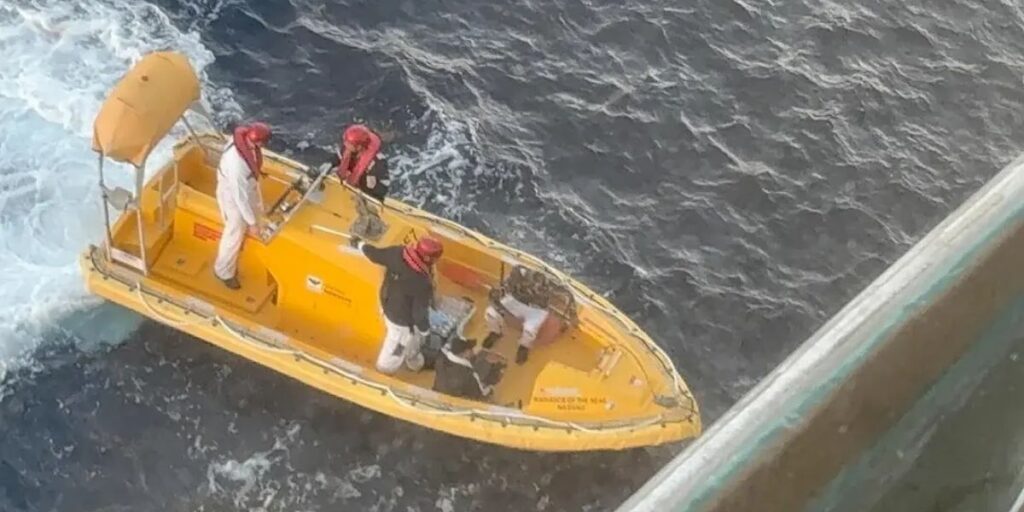 Radiance of the Seas crew in life vests aboard a yellow rescue boat assists a person at sea beside the cruise ship off the coast of Cuba.