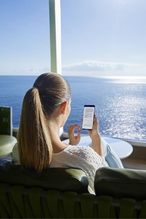 Cruise passenger using her phone at sea looking out towards the ocean, similar to how guests can access MSC Concierge through the MSC for Me app.