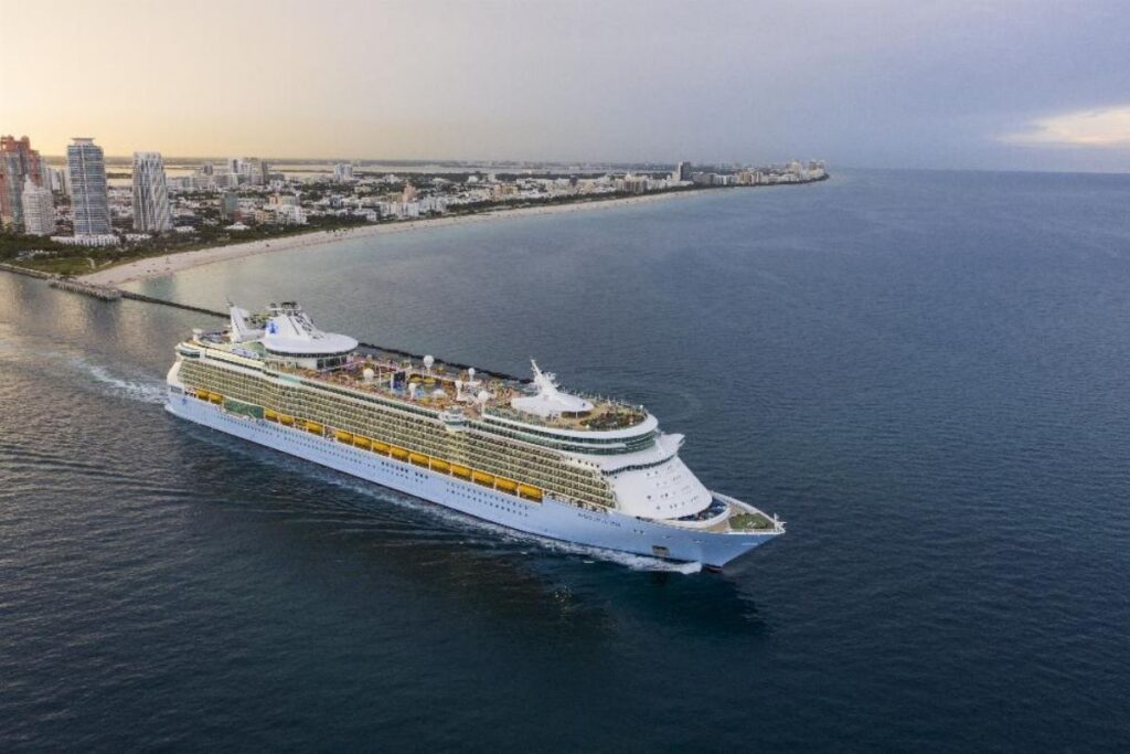 Royal Caribbean cruise ship sailing near the Miami coastline with the city and beach in the background.