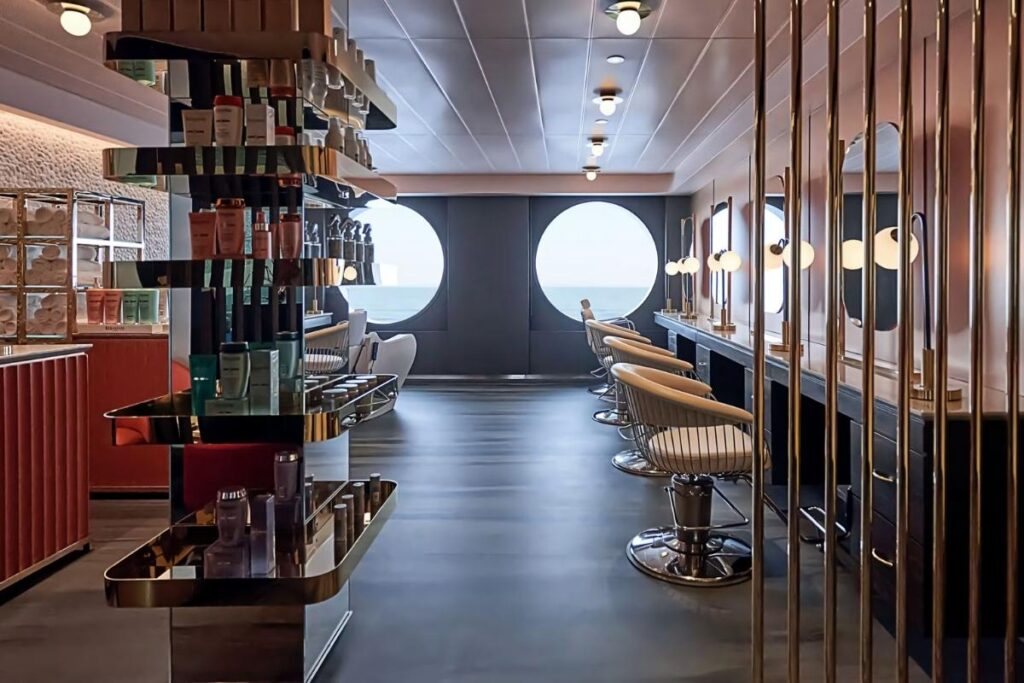 Modern Dry Dock hair salon, with styling chairs lined up beside mirrors, hair products displayed on shelves, and large round windows looking out to sea.