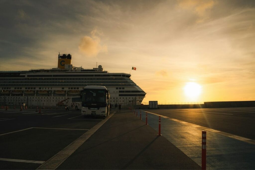 Large cruise ship docked at Naha port beside a passenger bus, with the sun setting over the harbor.