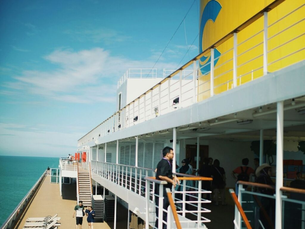 Passengers walking on the open deck of a Costa cruise ship near the yellow funnel.