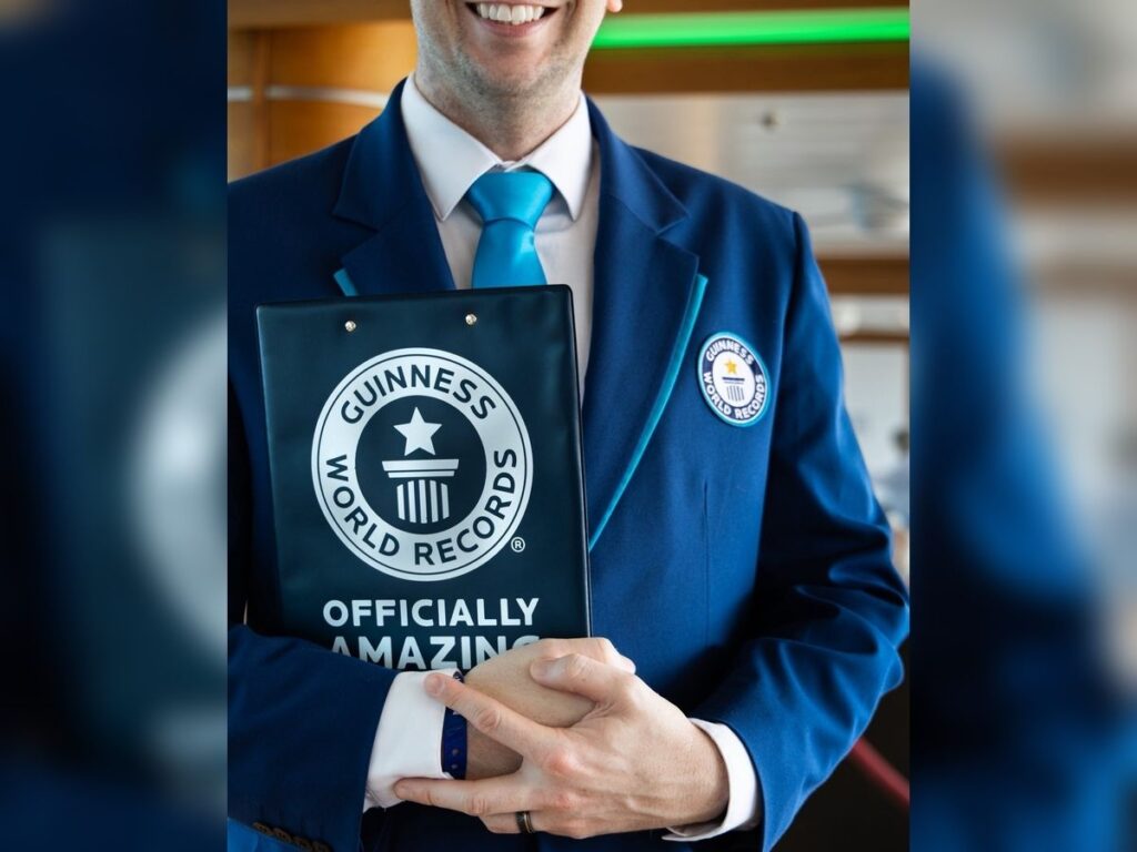 Guinness World Records adjudicator in a blue suit holds an “Officially Amazing” folder during a cruise ship event.