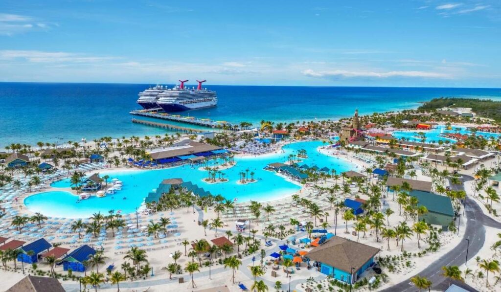 Aerial view of Celebration Key with two Carnival cruise ships docked at the pier and pools, beaches, and palm trees below.