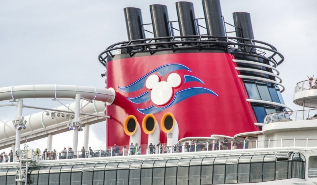 Disney Cruise Line ship funnel with the Mickey Mouse logo and passengers standing on deck.