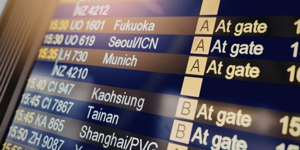 Close-up of an airport departure board showing flight destinations and “At gate” status updates.