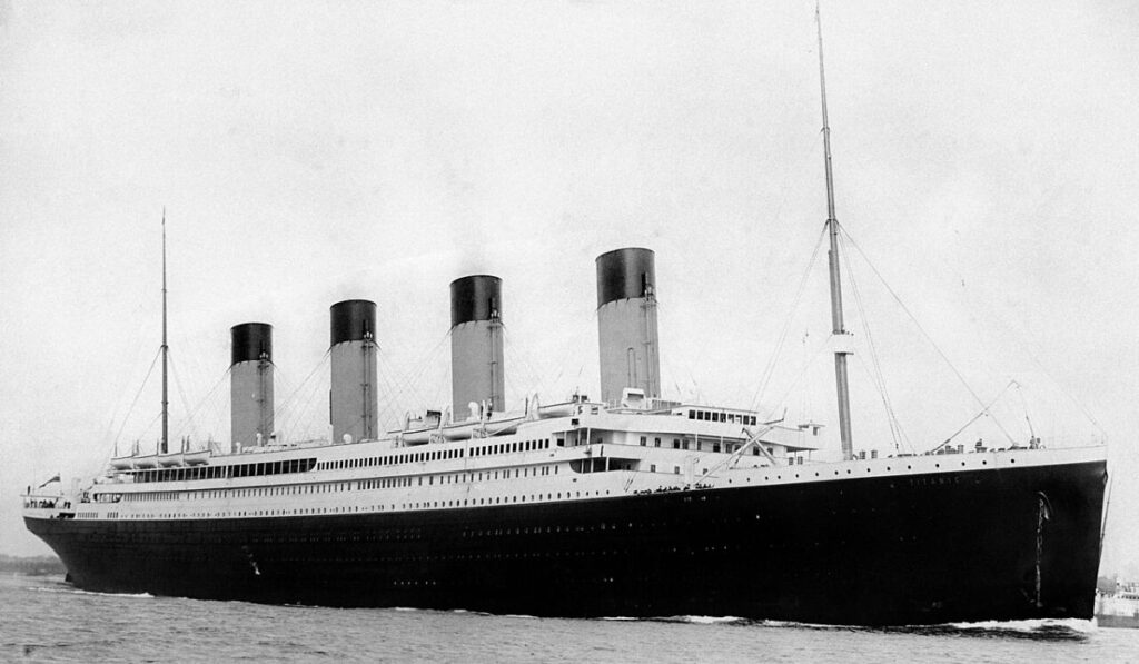 Black-and-white photograph of the RMS Titanic at sea with its four funnels visible.