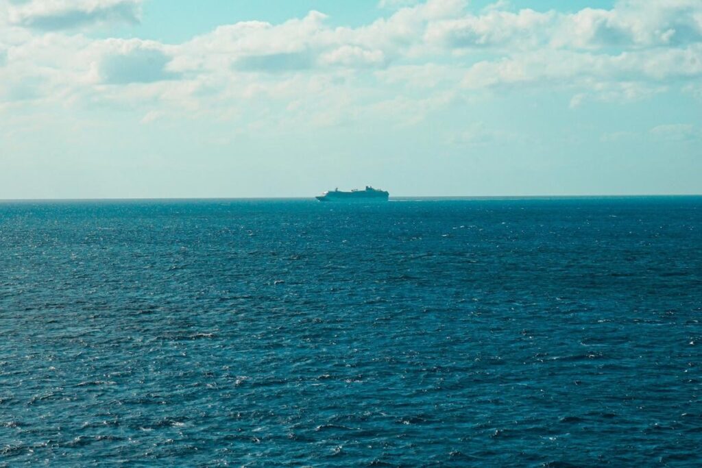 Distant cruise ship sailing across open ocean under a cloudy sky.