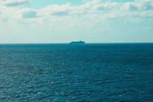 Distant cruise ship sailing across open ocean under a cloudy sky.