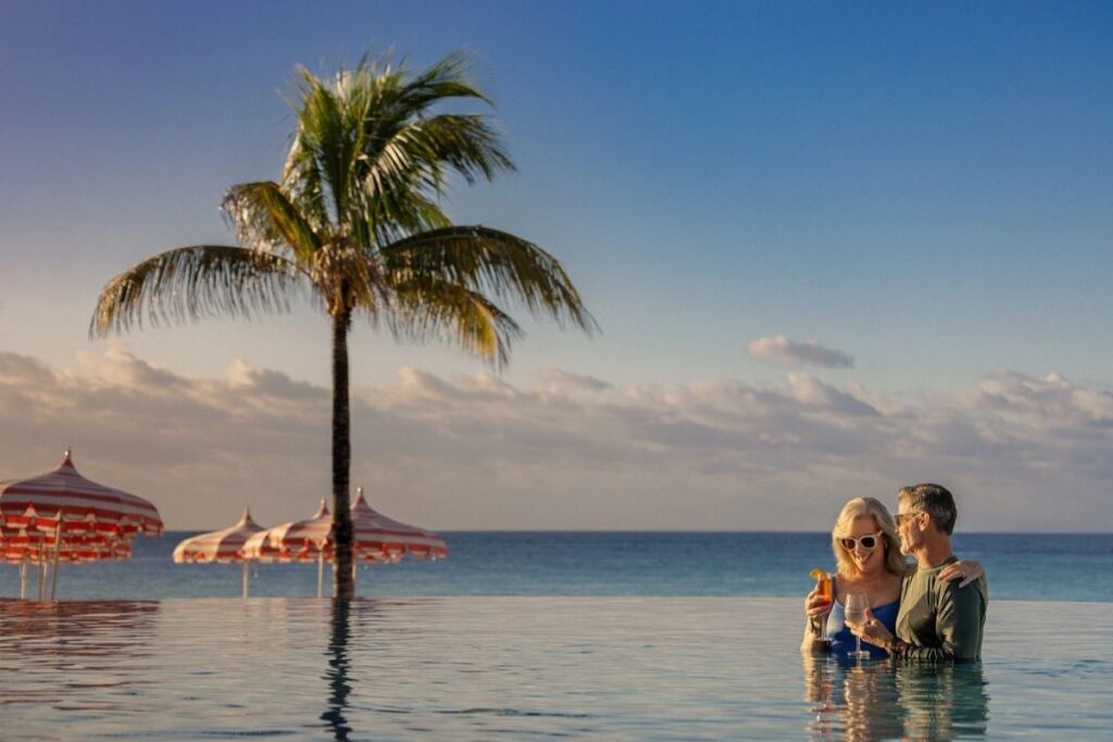 Couple relaxing with drinks in an infinity pool overlooking a tropical beach and ocean at Celebration Key in the Bahamas.