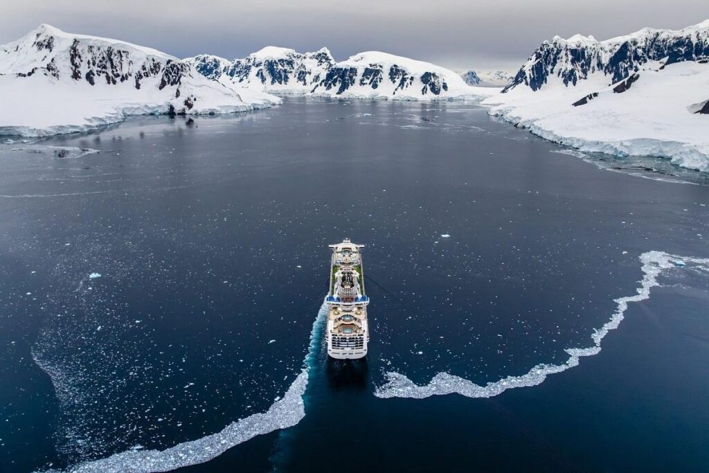 Princess cruise ship sailing through icy waters surrounded by snow-covered mountains in Antarctica.