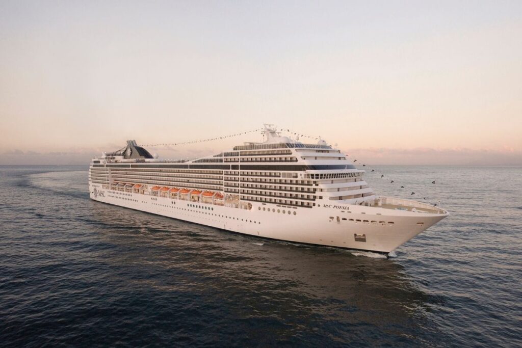 Wide view of MSC Poesia sailing at sea in calm water, showing the white cruise ship from the front starboard side under a pale evening sky.