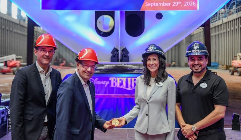 Four representatives wearing construction helmets pose with a commemorative coin at Disney Believe's keel-laying ceremony on September 29, 2026, at Meyer Werft shipyard.