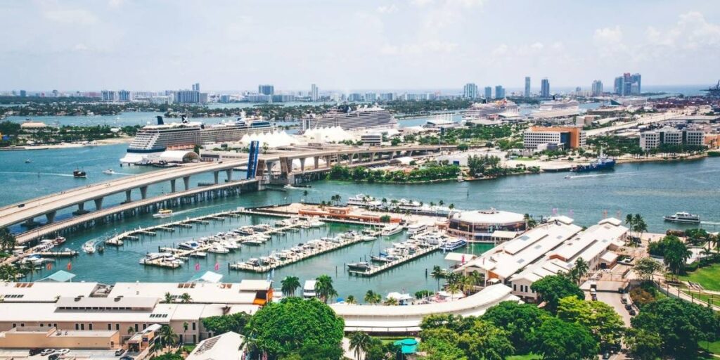 Aerial view of PortMiami with multiple cruise ships docked and the bridge approach over Biscayne Bay.