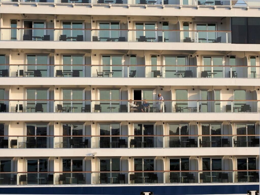 Rows of cruise ship balcony cabins with passengers standing on one balcony.