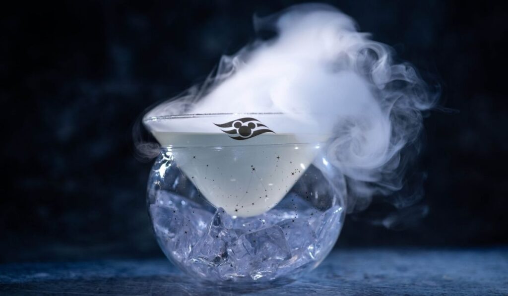 Moonshine cocktail served in a smoky glass with ice and the Disney Cruise Line logo at the Skygazers observatory-themed pub aboard Disney Believe.
