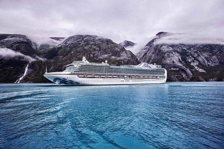 Ruby Princess cruise ship from Princess Cruises sailing in a scenic fjord surrounded by mountains in Alaska.