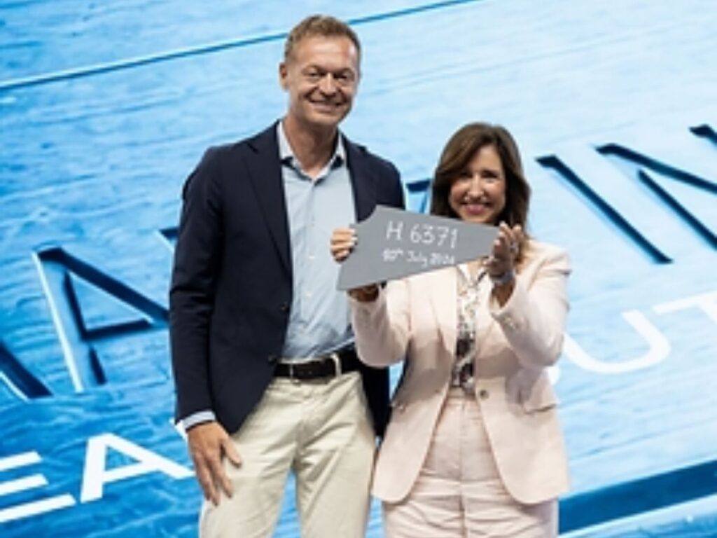 Two cruise executives at Carnival’s steel-cutting ceremony hold a metal plate marked H6371 to mark the start of construction for Carnival Destiny.
