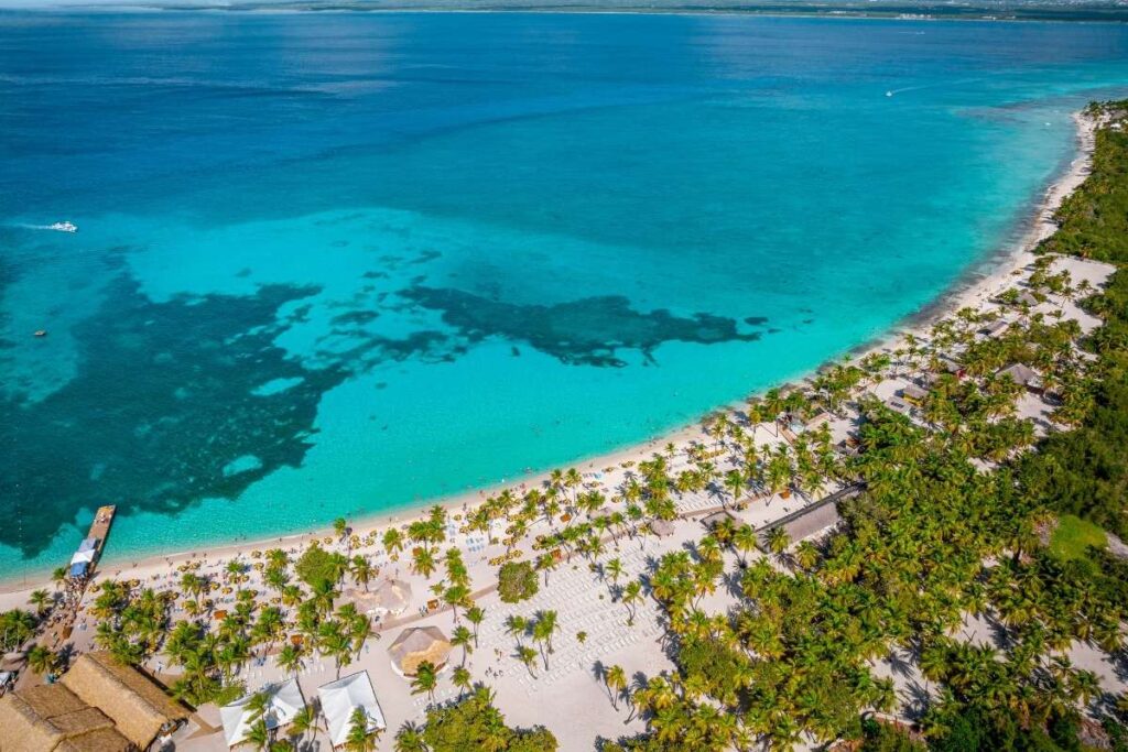 Aerial view of Catalina Island in the Dominican Republic, showing a long white-sand beach, palm trees, lounge areas, and clear turquoise Caribbean water.