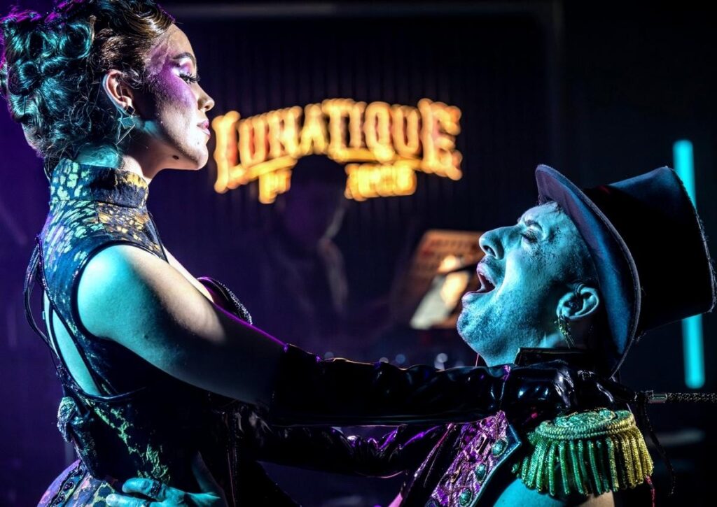 Performer in glittering costume stands over a singer in a top hat during Norwegian Luna’s adults-only LunaTique show.