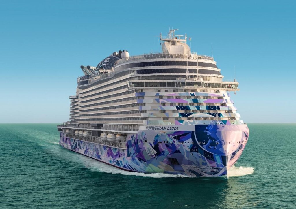 Norwegian Luna sails at sea, showing the cruise ship’s colorful hull artwork from the front.