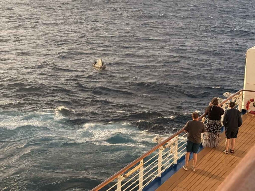 Passengers on the Regal Princess look out over choppy water toward a tiny makeshift sailboat during the ship’s rescue diversion.