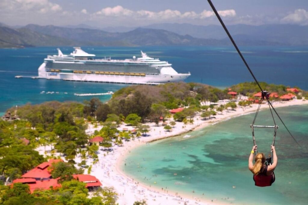 Cruise passenger ziplining over Labadee, Haiti, with a Royal Caribbean ship anchored offshore and the beach below.