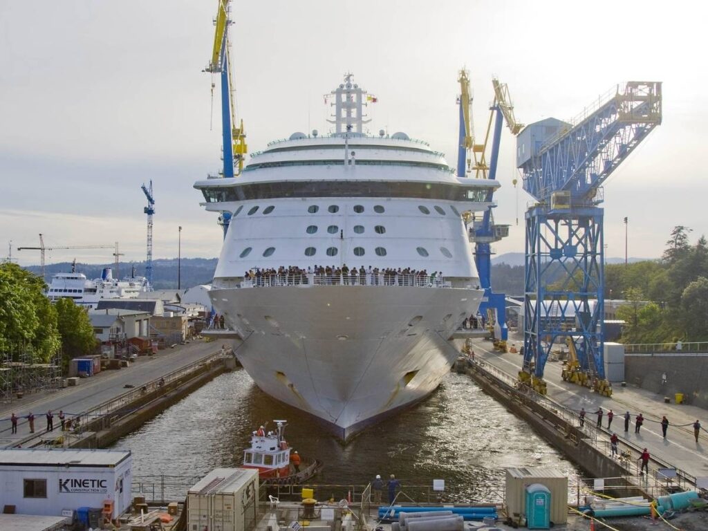 Front view of Radiance of the Seas positioned in dry dock with cranes and workers visible along the dock.