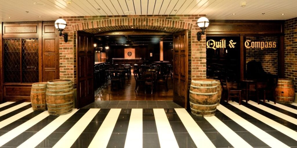 Quill & Compass pub doorway onboard Radiance of the Seas, featuring barrels and a brick-front entrance.