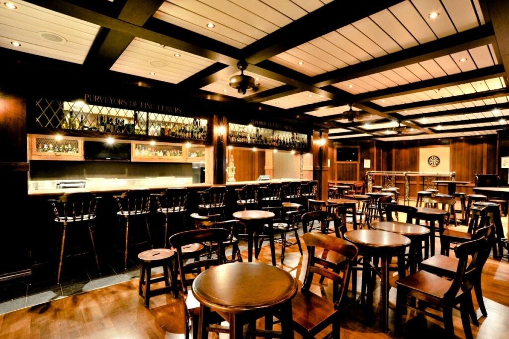 Empty Quill & Compass pub with long bar, wooden tables, warm lighting, and a dartboard at the back.