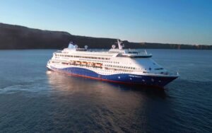Celestyal Discovery sailing at sea near a rocky coastline.