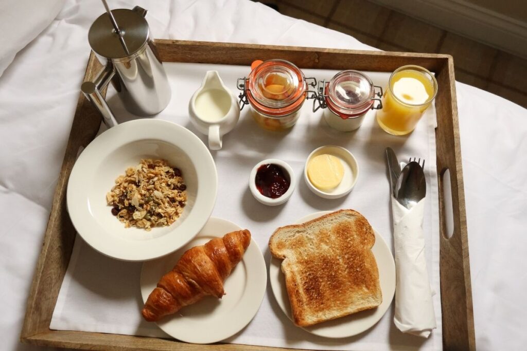 Room service breakfast on a wooden tray, including toast, croissant, cereal, and coffee