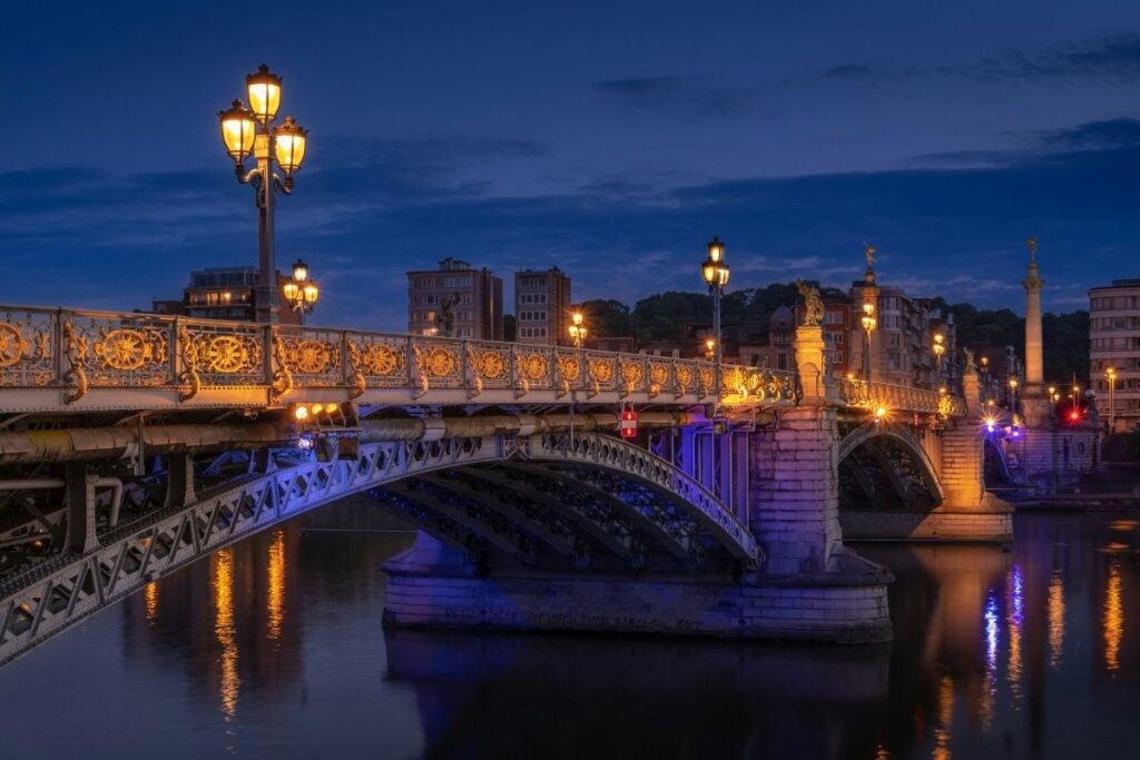 Ornate bridge lit up over a river in Liege, Belgium at dusk.