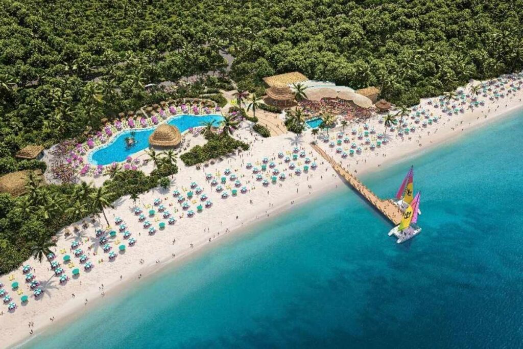 Aerial view of Royal Beach Club Cozumel with a sandy beach, pool area, loungers and colorful sailboats along the shoreline.