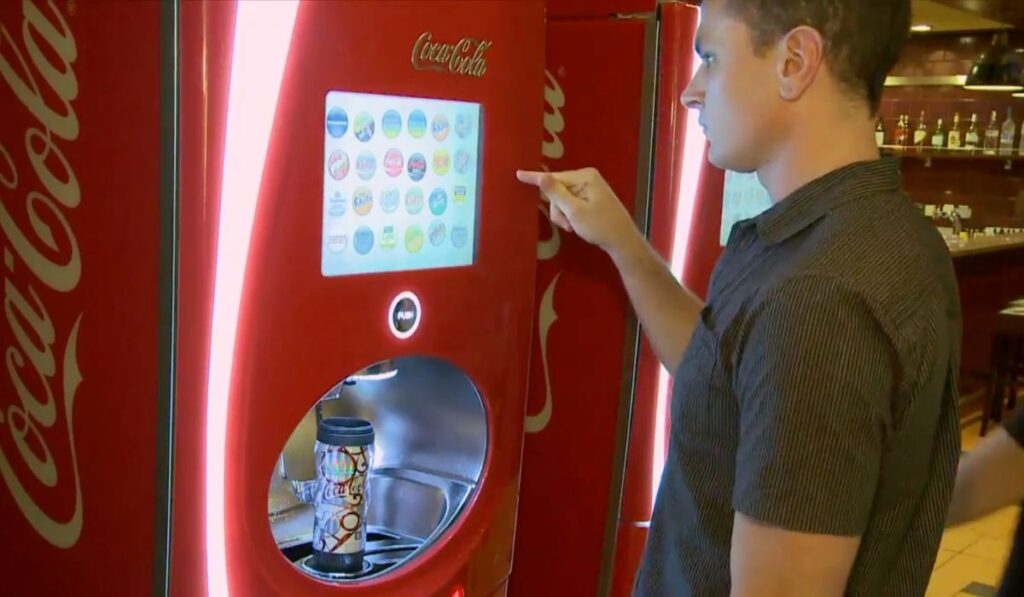 A Royal Caribbean cruise guest uses a Coca-Cola Freestyle machine to refill a souvenir cup at a self-serve soda station.
