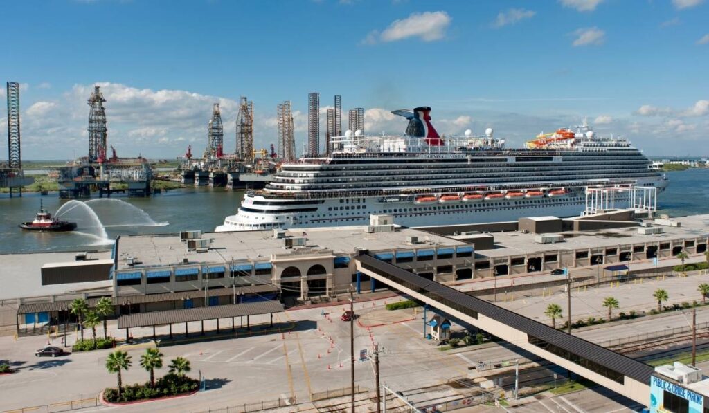 Carnival cruise ship docked at the Port of Galveston in Texas with a tugboat spraying water nearby.