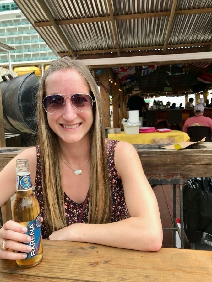 Woman holding a beer at an outdoor beach bar during a cruise stop.
