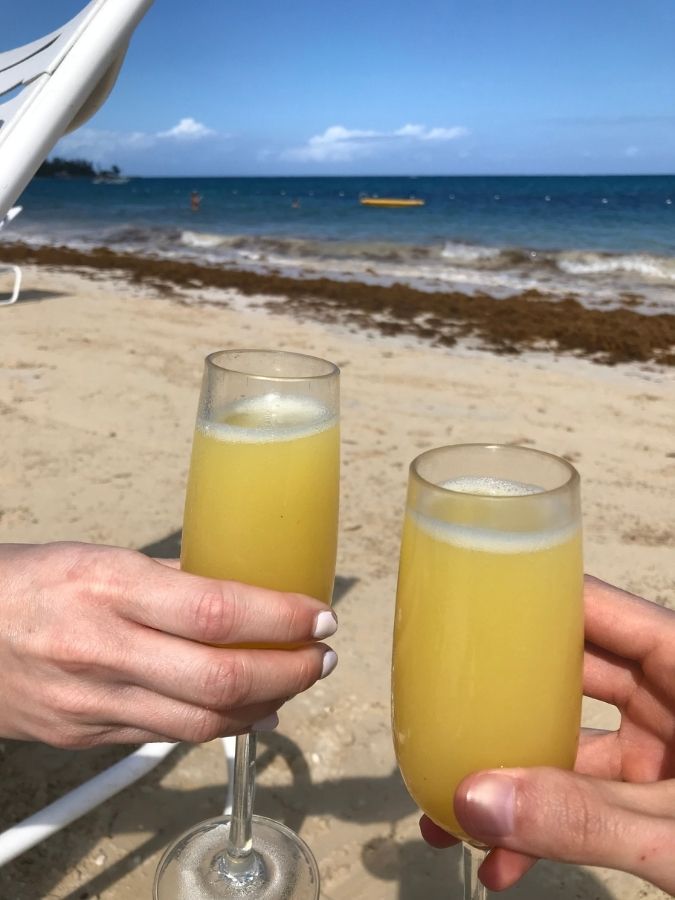 Two glasses of tropical drinks held up on a sunny beach.