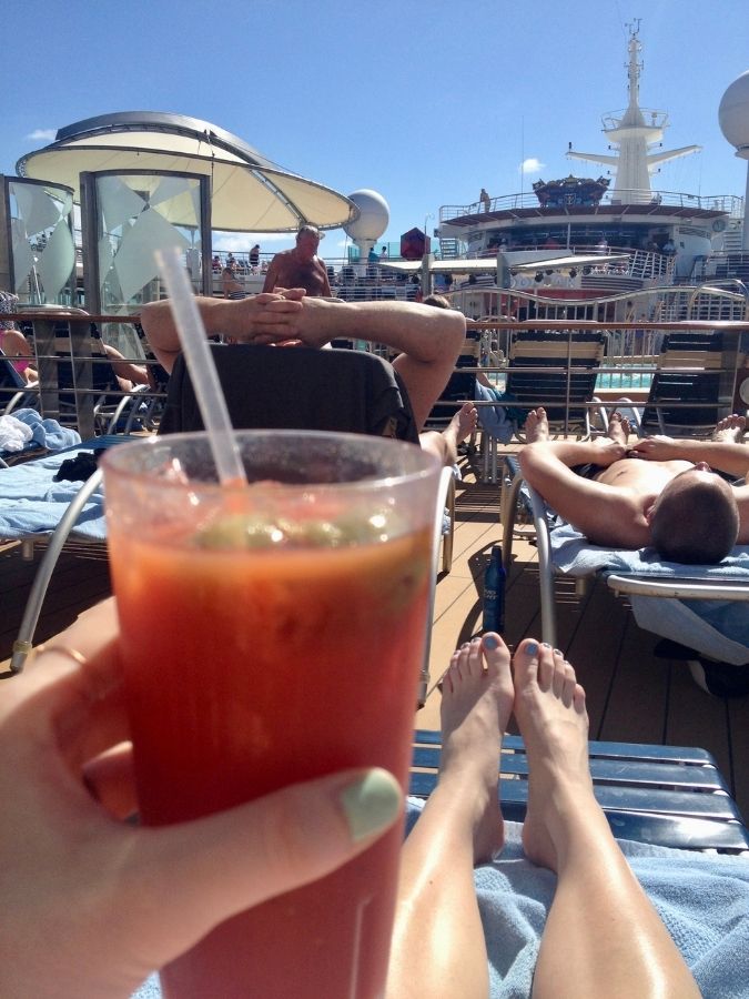 Bloody Mary cocktail held beside a cruise ship pool deck from lounge chair.