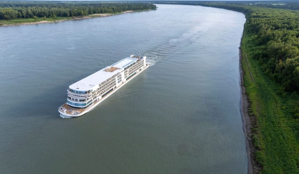 An aerial view of a Viking river cruise ship cruising along the Mississippi River bordered by green forest.