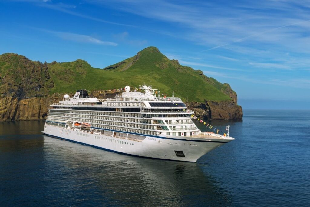 Viking Sky sails beside a rugged green island in Iceland surrounded by calm blue water on a clear day.