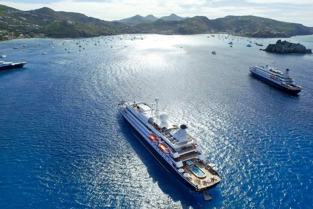 Aerial view of two SeaDream yachts anchored in a Caribbean bay surrounded by sailboats and green hills.