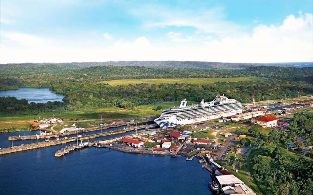 Coral Princess cruise ship passing through the Panama Canal, surrounded by lock chambers, green forest, and calm blue water.