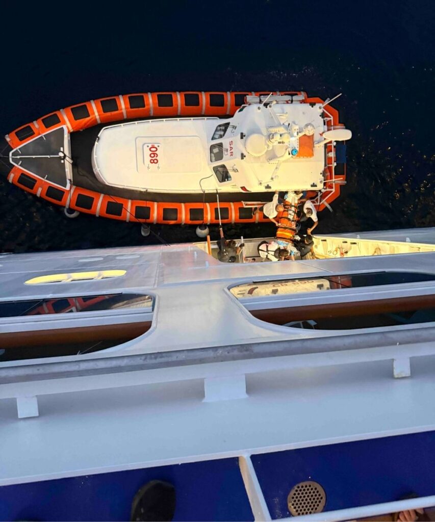 Italian Coast Guard rescue boat alongside a cruise ship during a nighttime medical evacuation.