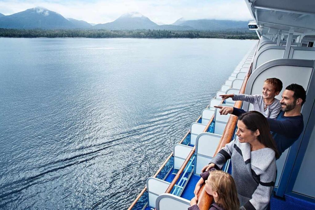 Family on their cruise balcony pointing out the coastal scenery during an Alaska-style sailing.