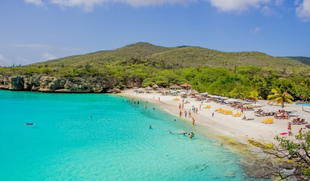 Cruise guests relaxing and swimming at a sunny Caribbean beach with clear turquoise water.